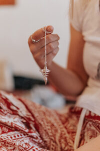 Eine Person hält ein Metallpendel an einer Kette und lässt es schwingen, während sie es für energetische Arbeit oder Entscheidungen verwendet.